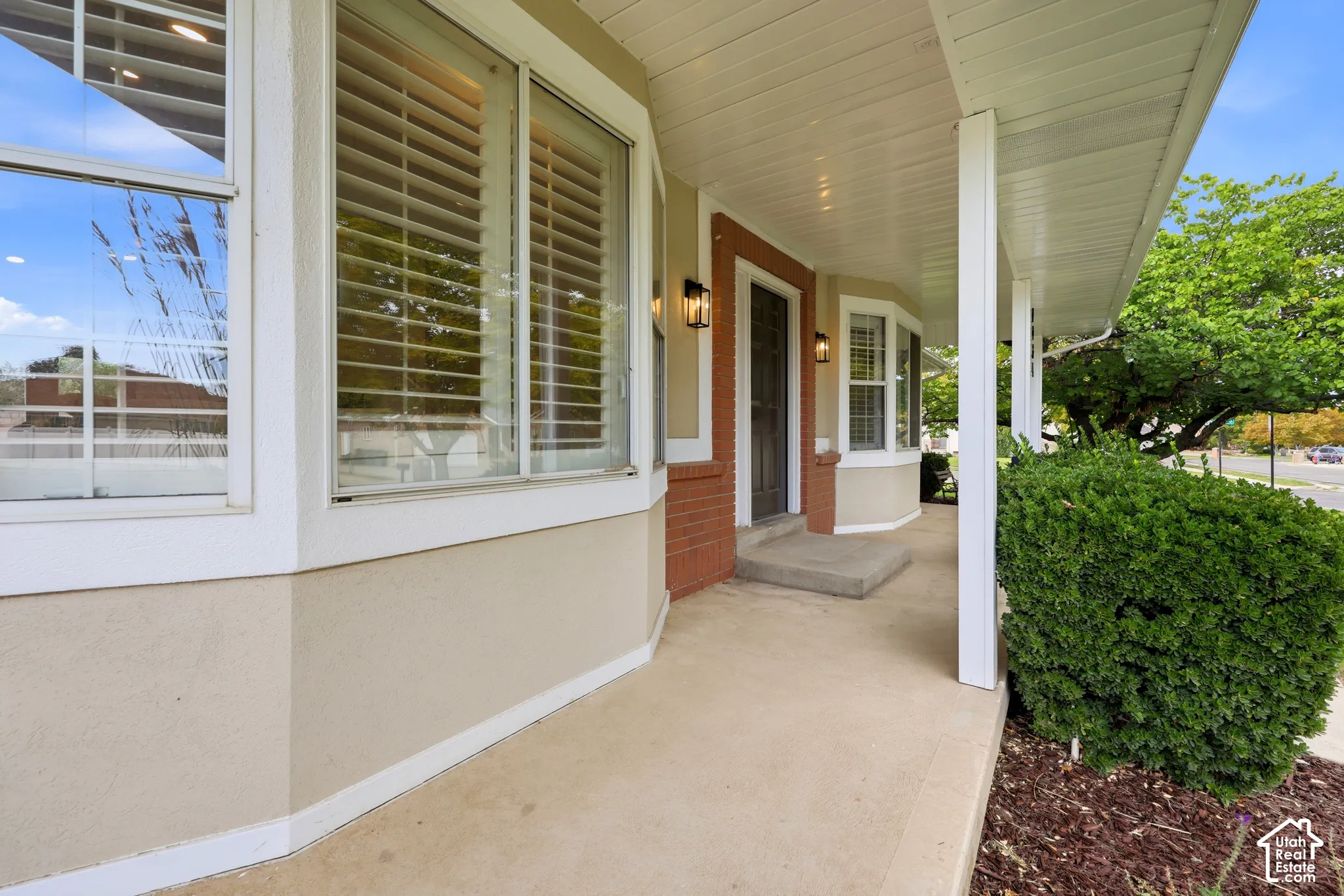 Covered front porch with white columns, stucco exterior, brick accent detailing, a bay window, and exterior wall sconces