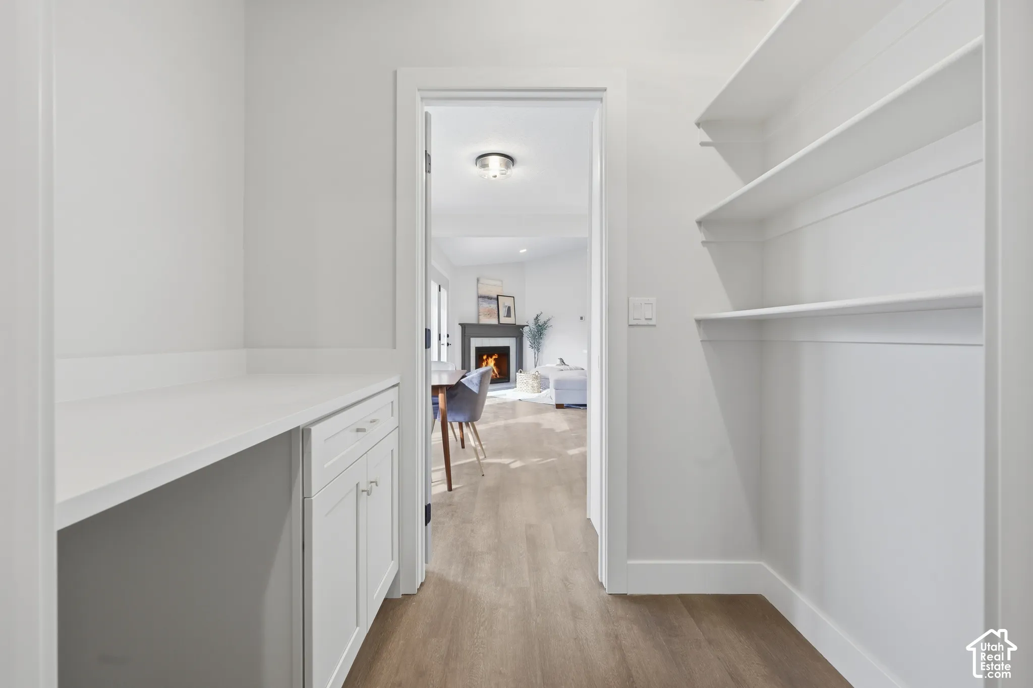 Built-in white shelving, wood-finish flooring, white cabinetry with silver hardware, and a white countertop