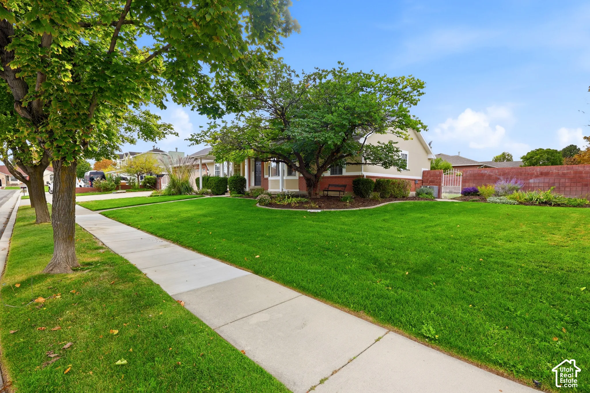 Expansive front lawn with mature shade trees, concrete sidewalk, and a brick privacy wall