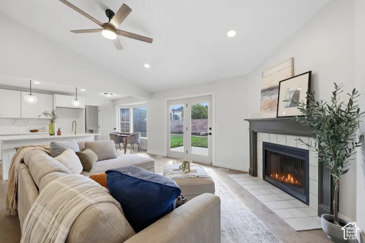 Vaulted ceiling with a ceiling fan, recessed lighting, fireplace with a tiled hearth and wood mantle, French doors to the exterior, and wood-finish flooring
