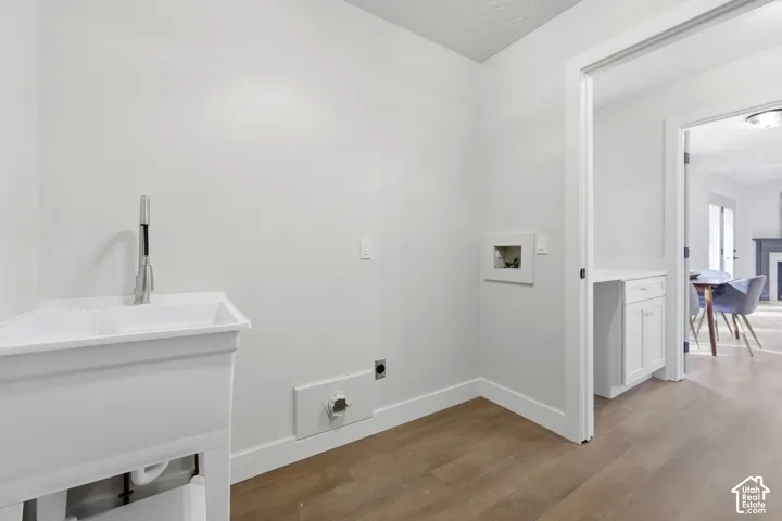 Utility sink with a pull-down faucet, wood-finish flooring, and white cabinetry