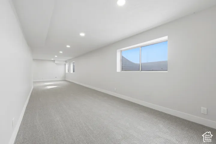 Recessed lighting illuminates the expansive room with light gray carpeting and white walls
