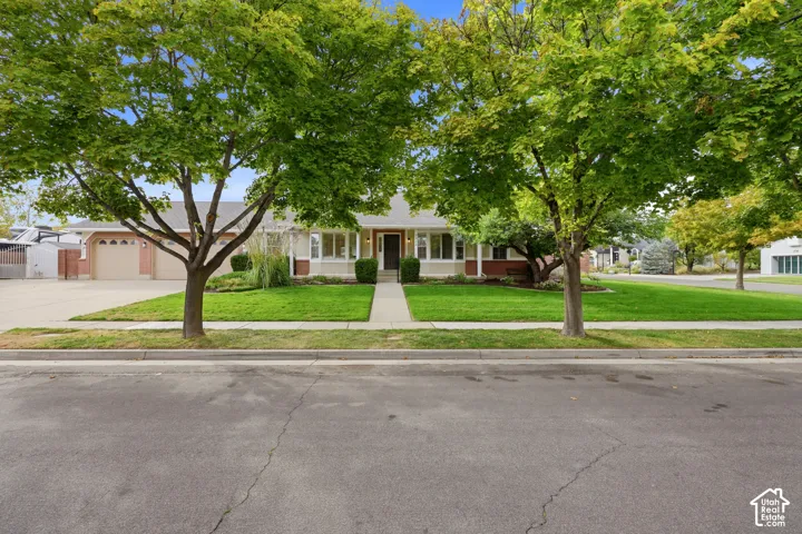 Single-story residence featuring a two-car garage, manicured lawn, and mature trees