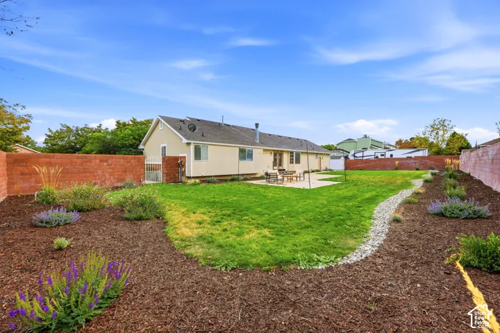Expansive backyard featuring a manicured lawn, concrete patio, a rock-lined dry creek bed, and landscaped garden beds with mulch and plantings