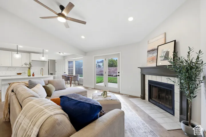 Vaulted ceiling with a contemporary ceiling fan, built-in fireplace with a tile surround, and French doors opening to an exterior