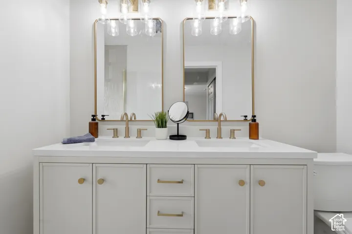 Double vanity with integrated sinks, white countertop, gold-finish hardware, and dual gold-framed mirrors