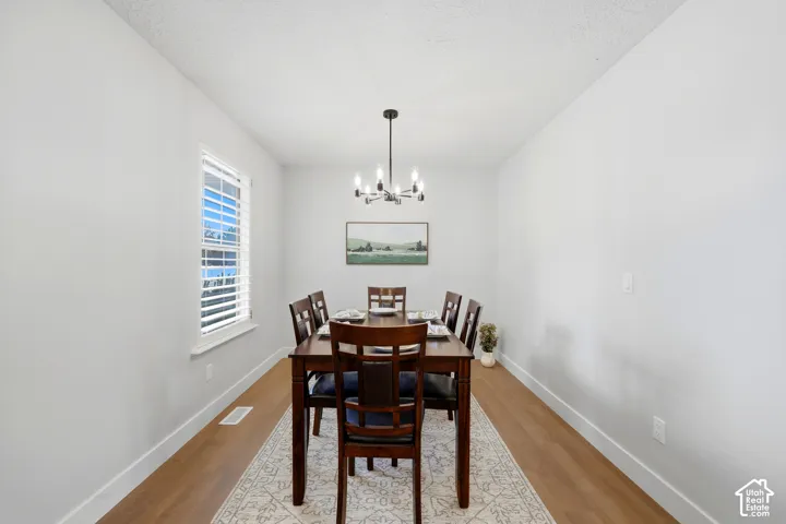 Recessed dining space featuring a window with white blinds, wood-finish flooring, and a contemporary chandelier