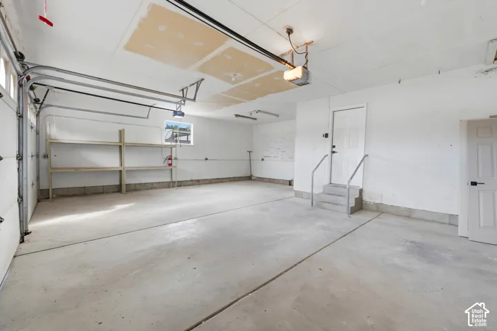 Spacious garage featuring a concrete floor, built-in shelving, two entry doors, and an overhead garage door
