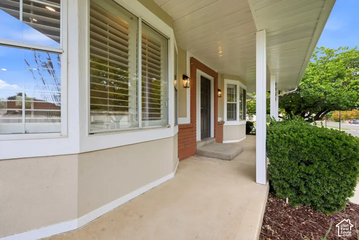 Covered front porch with white columns, stucco exterior, brick accent detailing, a bay window, and exterior wall sconces
