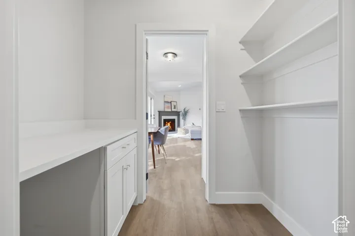 Built-in white shelving, wood-finish flooring, white cabinetry with silver hardware, and a white countertop