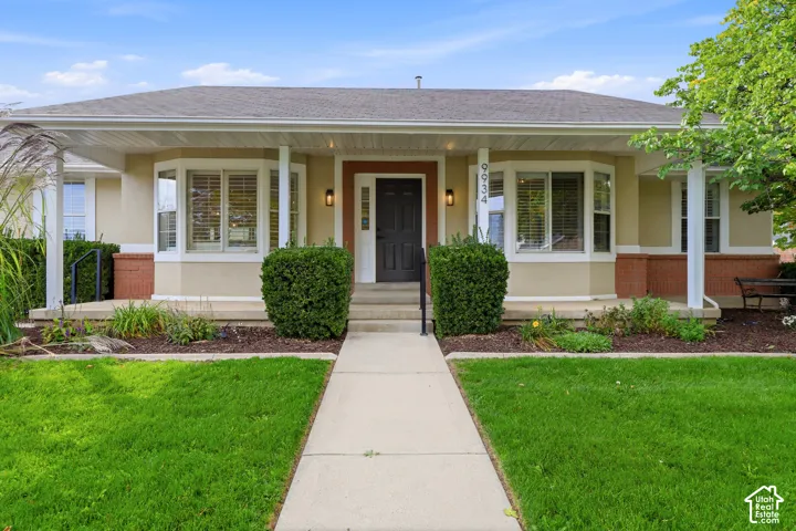 Stucco exterior with a covered porch, bay windows, mature landscaping, a concrete walkway, and a dark entry door