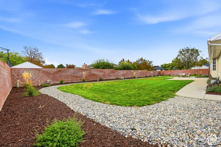 Expansive backyard featuring a large lawn, brick perimeter wall, concrete patio, gravel pathway, and landscaped beds with mulch