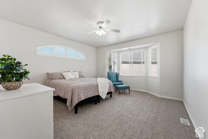 Primary suite with neutral tone carpeting, ceiling fan, and bay window