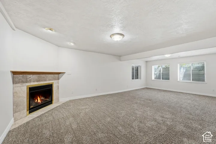 Spacious basement living room with neutral-toned carpeting and a corner gas fireplace