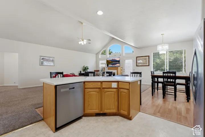 Open-concept kitchen and dining area featuring a curved wood-finish cabinetry island with stainless steel appliances, white countertops and vaulted ceilings