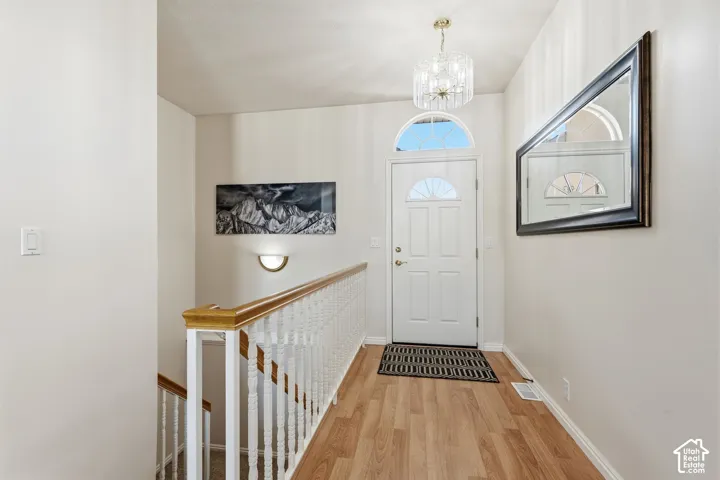 Entryway featuring wood-finish flooring, a decorative chandelier, and a white front door with an arched transom window