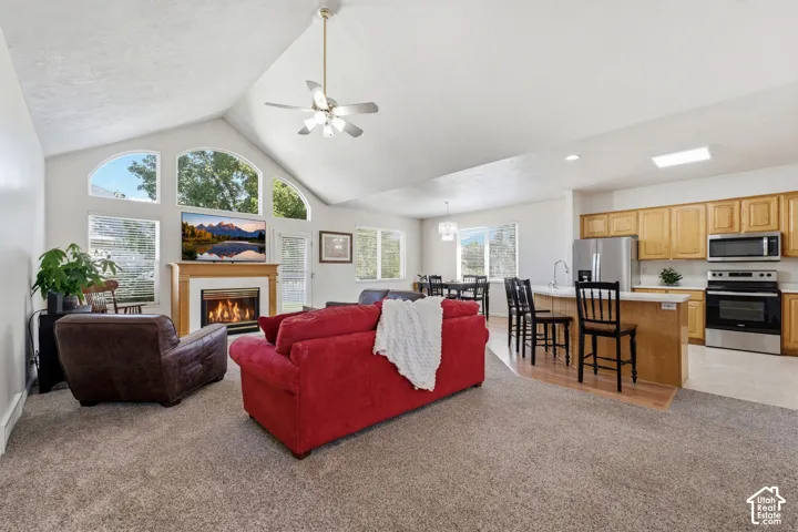Vaulted ceiling with a ceiling fan, fireplace, kitchen island, and lots of natural light