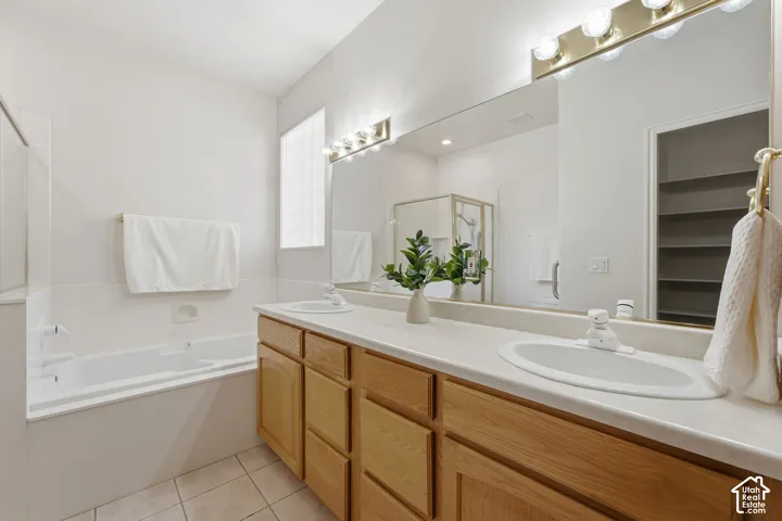 Primary en suite with dual sink vanity, wood-finish cabinetry, and large tub