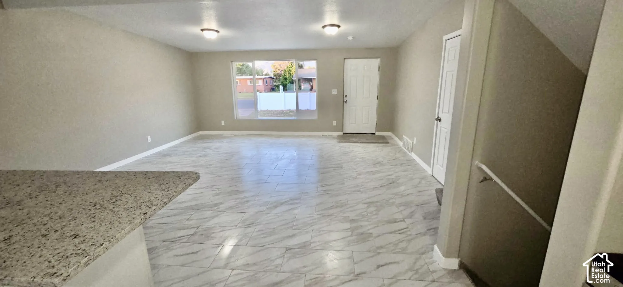 Spacious living area featuring light-toned walls, large windows, and a white entrance door