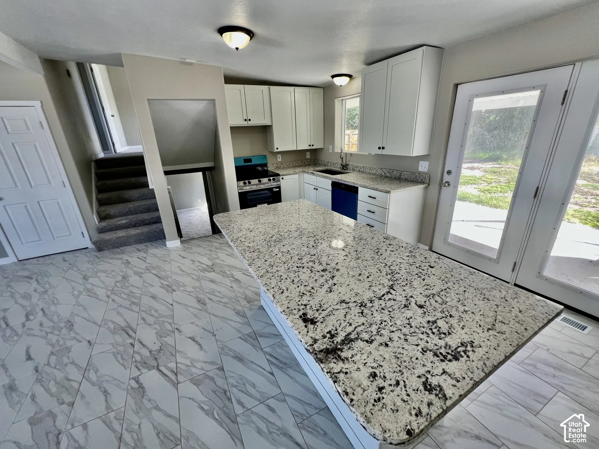 Spacious kitchen featuring an extended island with a light-toned countertop, white cabinetry with dark hardware, a stainless steel gas range, and a full-light patio door
