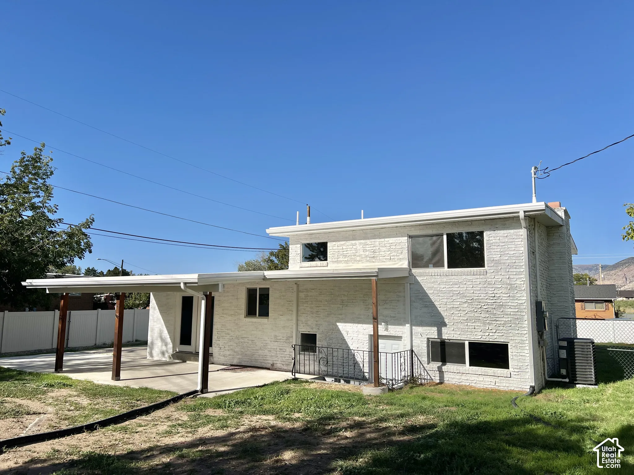 White brick exterior with multiple windows, a covered patio featuring wood-toned posts, and a concrete patio