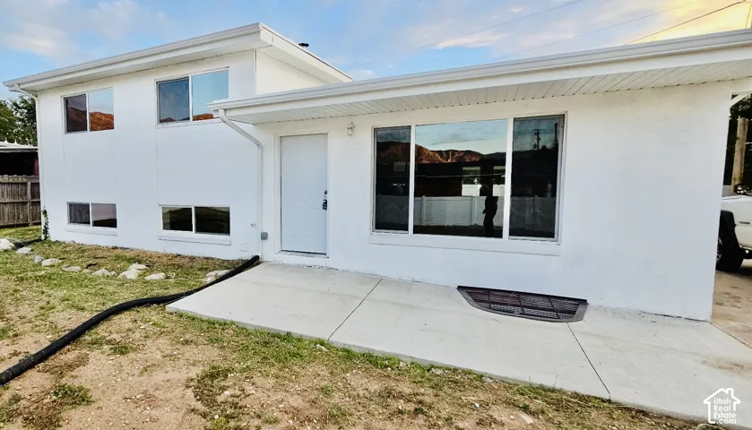 White stucco exterior with multiple windows, a concrete patio, and a foundational window well
