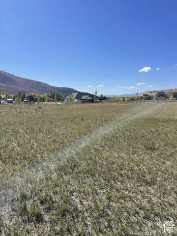 Expansive grassy lot with mountain scenery and distant residential structures