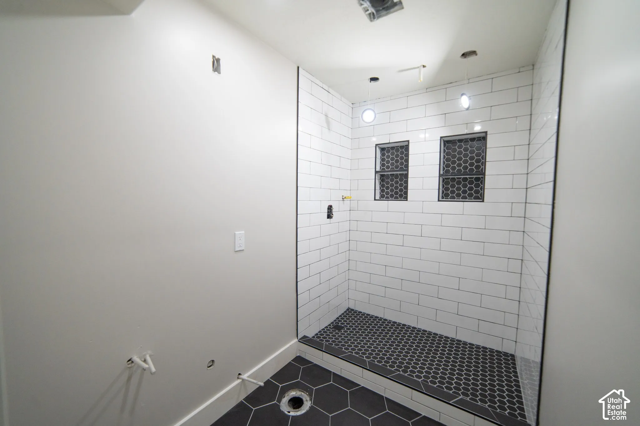 Walk-in shower with white subway tile, integrated tiled niches, and a black hexagonal tile floor