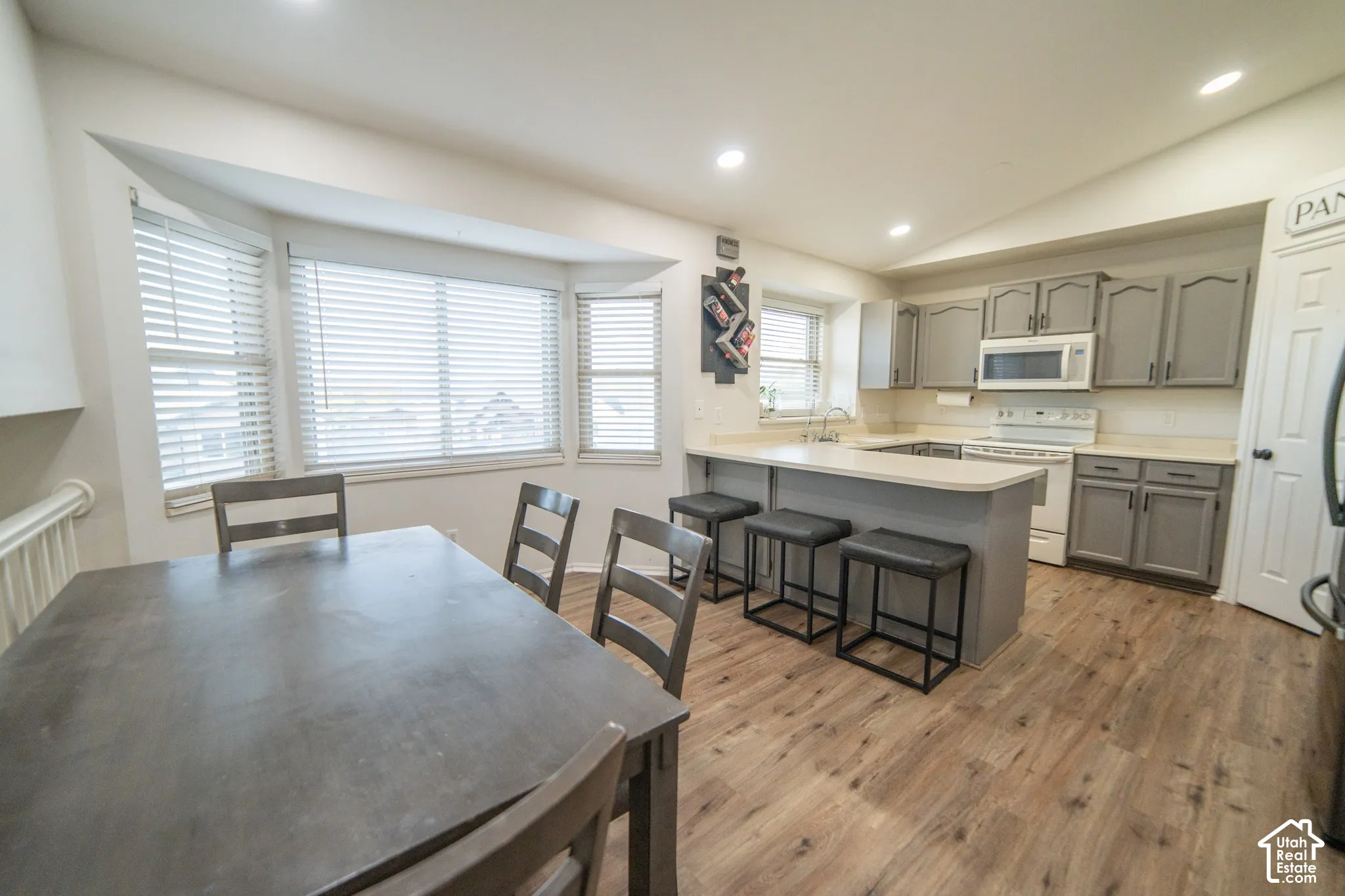 Kitchen featuring wood-finish flooring, recessed lighting, gray cabinetry, white appliances, and a breakfast bar with seating