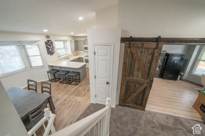 Open-concept living space with wood-finish flooring, a kitchen island with seating, recessed lighting, and a rustic barn door