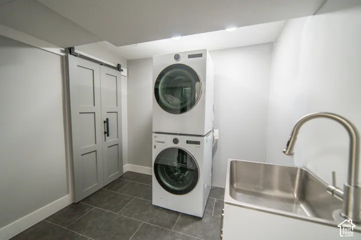 Barn door, stacked laundry appliances, stainless steel utility sink, pull-down faucet, and tiled flooring