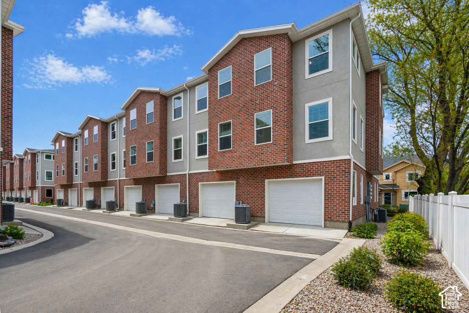 Brick and stucco exterior, multiple garage doors, white vinyl fencing, mature landscaping, paved drive
