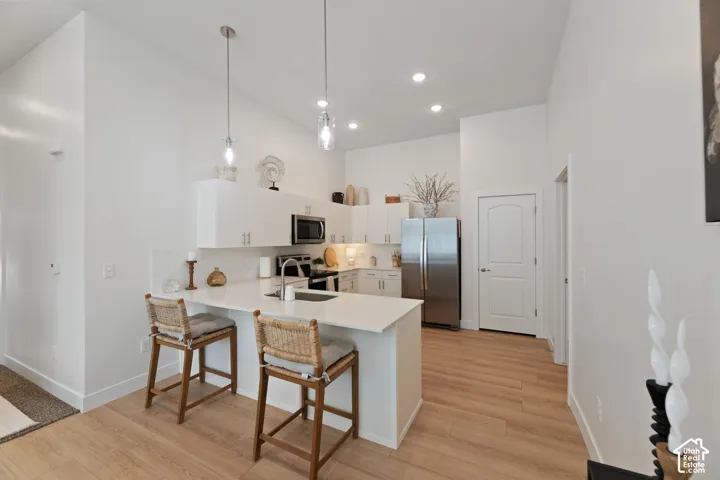 Kitchen featuring a large island with counter seating, stainless steel appliances, white cabinetry, and wood-finish flooring