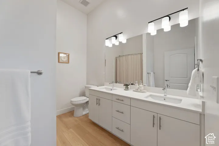 Master Bath Dual vanity with white cabinetry and chrome hardware, light-toned wood-finish flooring, and a full-width mirror with contemporary light fixtures