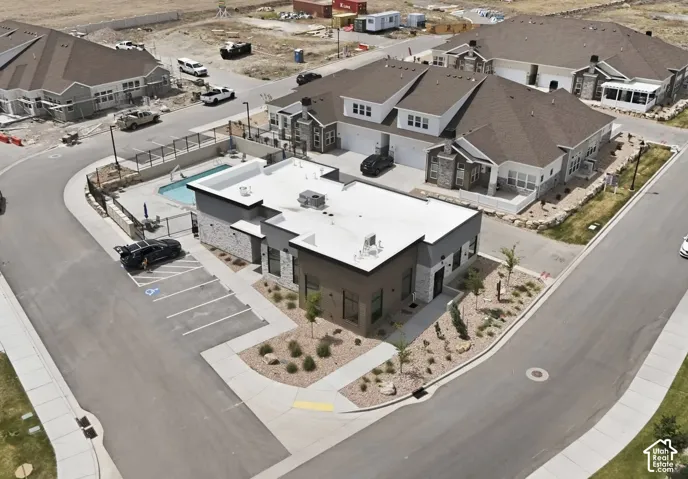Community clubhouse with an outdoor swimming pool, paved parking, and landscaped grounds