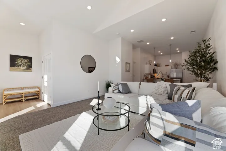 Recessed ceiling lighting, 11' vaulted ceiling, white walls, wood-finish flooring, and a kitchen with stainless steel appliances