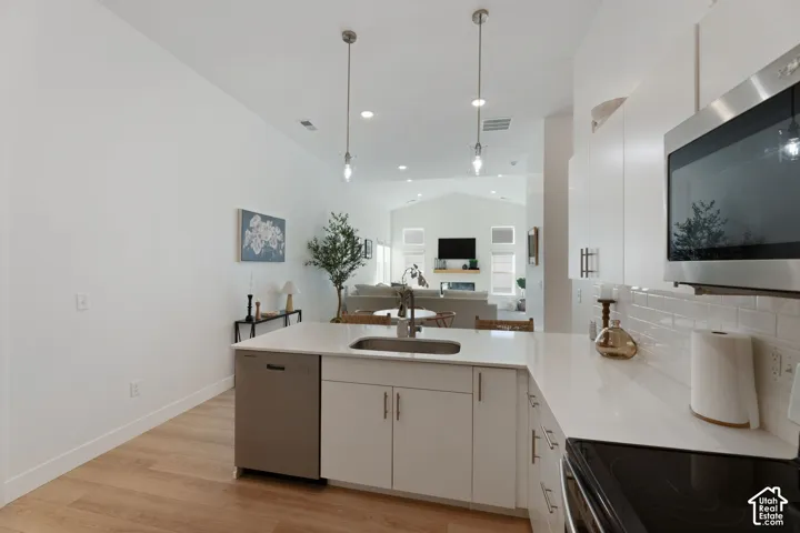 Kitchen featuring white cabinetry, light-toned countertops, stainless steel appliances, and wood-finish flooring