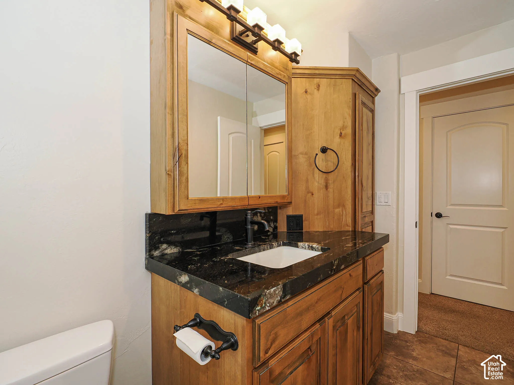 Wood-finish cabinetry with a black stone countertop, featuring an integrated sink and black faucet