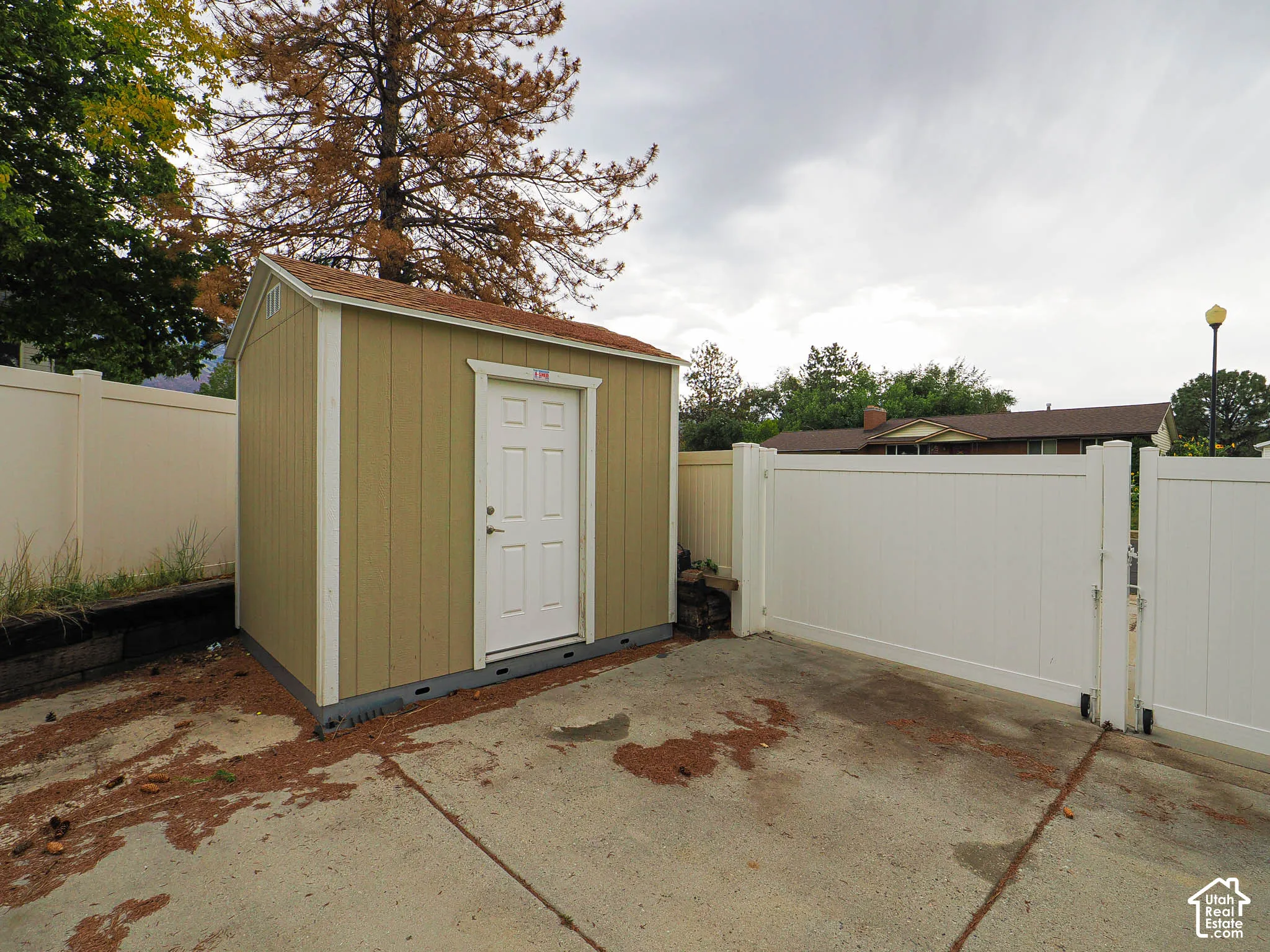 Outdoor storage shed with a panel door, accompanied by a white privacy fence and concrete paving
