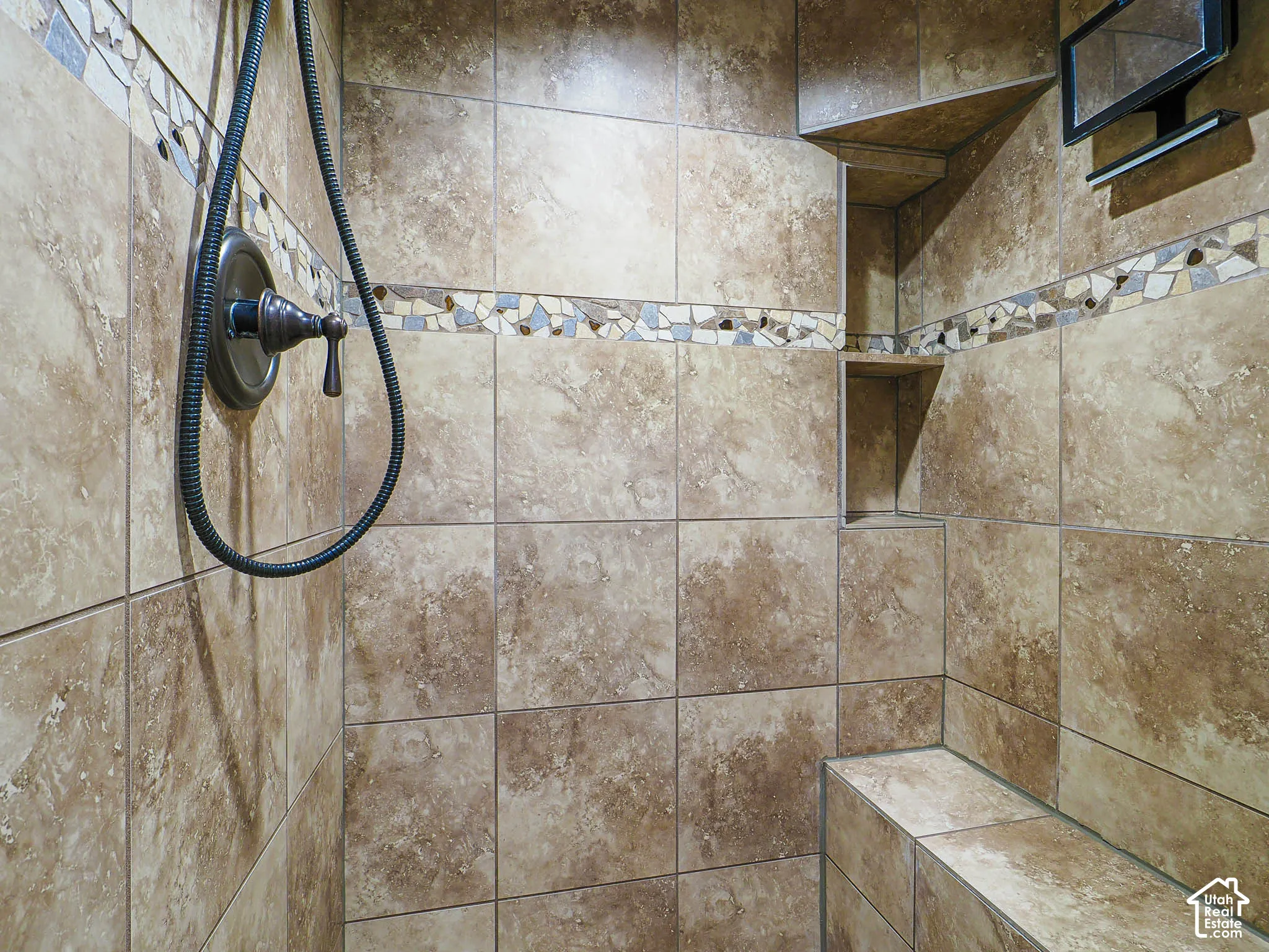 Tiled shower featuring a built-in bench, recessed niches, decorative mosaic band, and bronze-finish fixtures