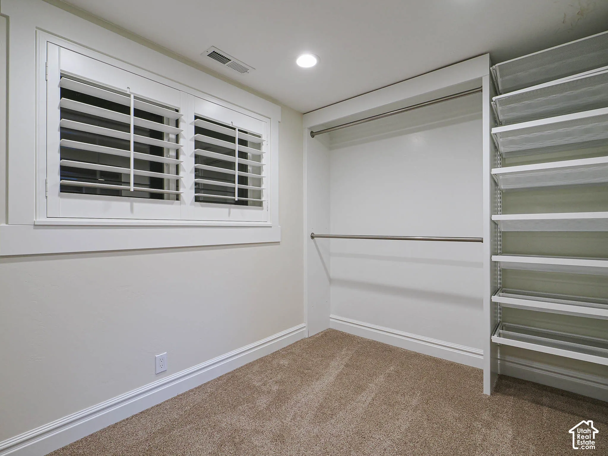 Recessed lighting, warm carpet flooring, white window shutters, and a built-in closet organization system with shelving and hanging rods