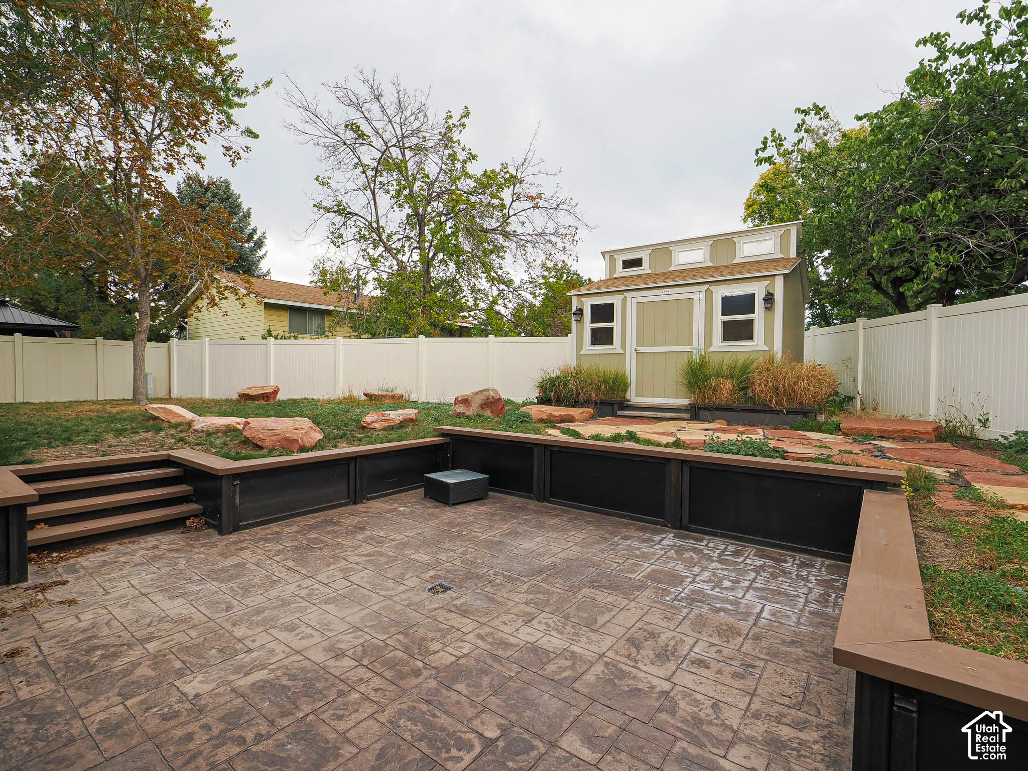 Stamped concrete patio with multi-level landscaping, featuring a built-in storage shed and a white privacy fence