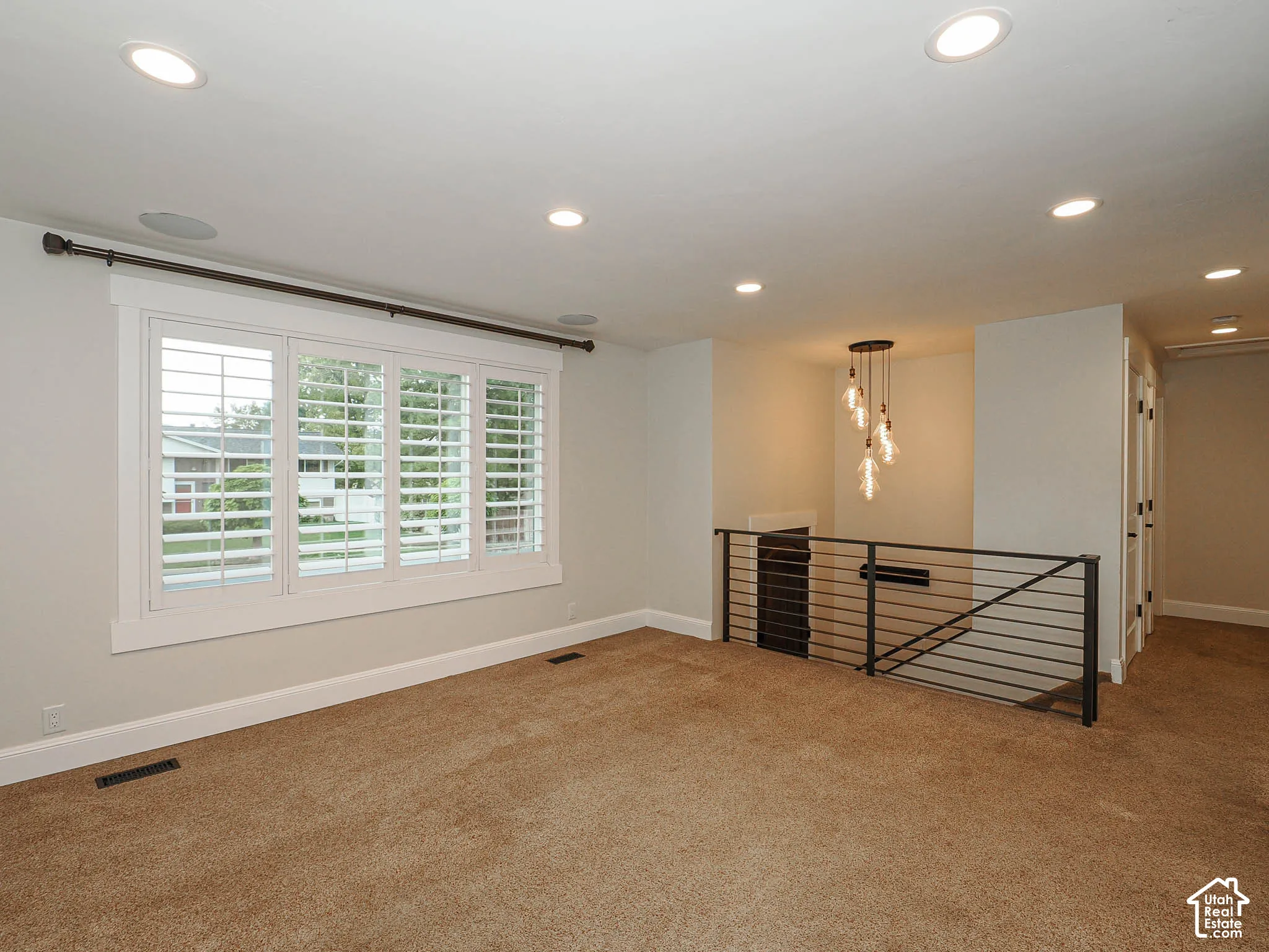 Plantation shutters, recessed lighting, and a modern industrial-style chandelier illuminate this space, featuring a sleek metal railing