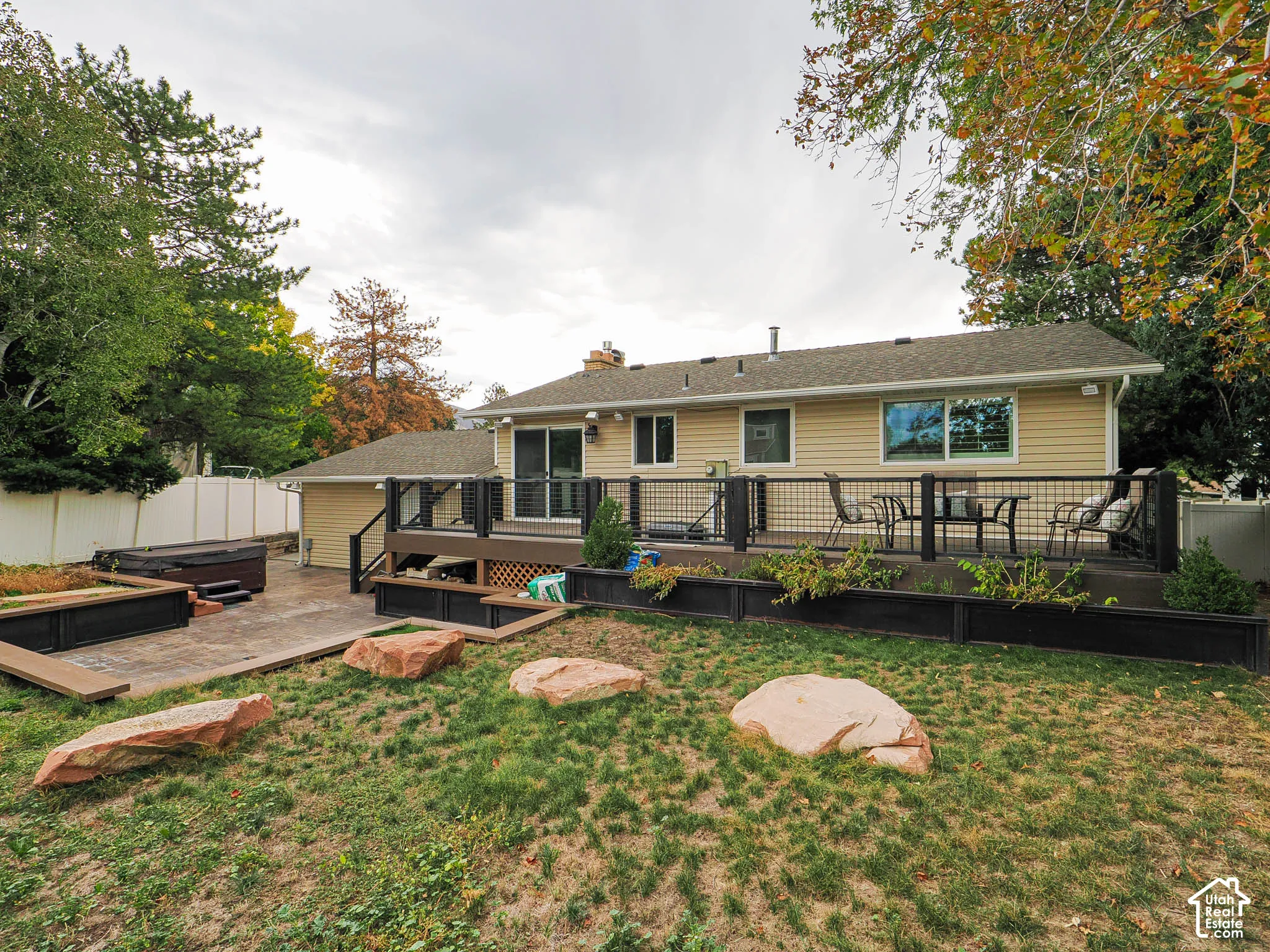 Expansive outdoor deck with a metal railing system, sliding glass door access, and an adjacent patio with a built-in spa