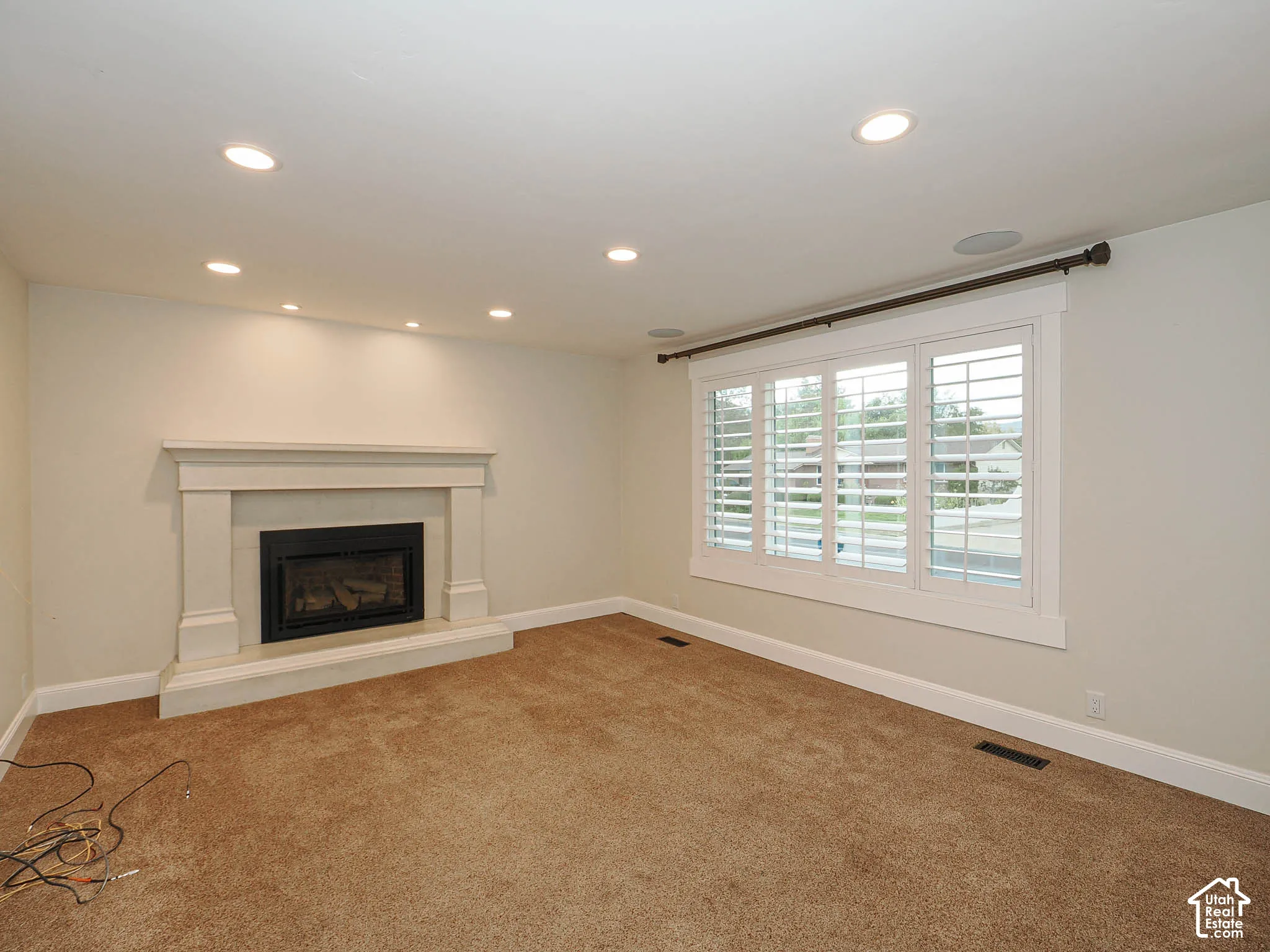 Recessed lighting, a fireplace with a mantel, a window with plantation shutters, and light-toned carpeting