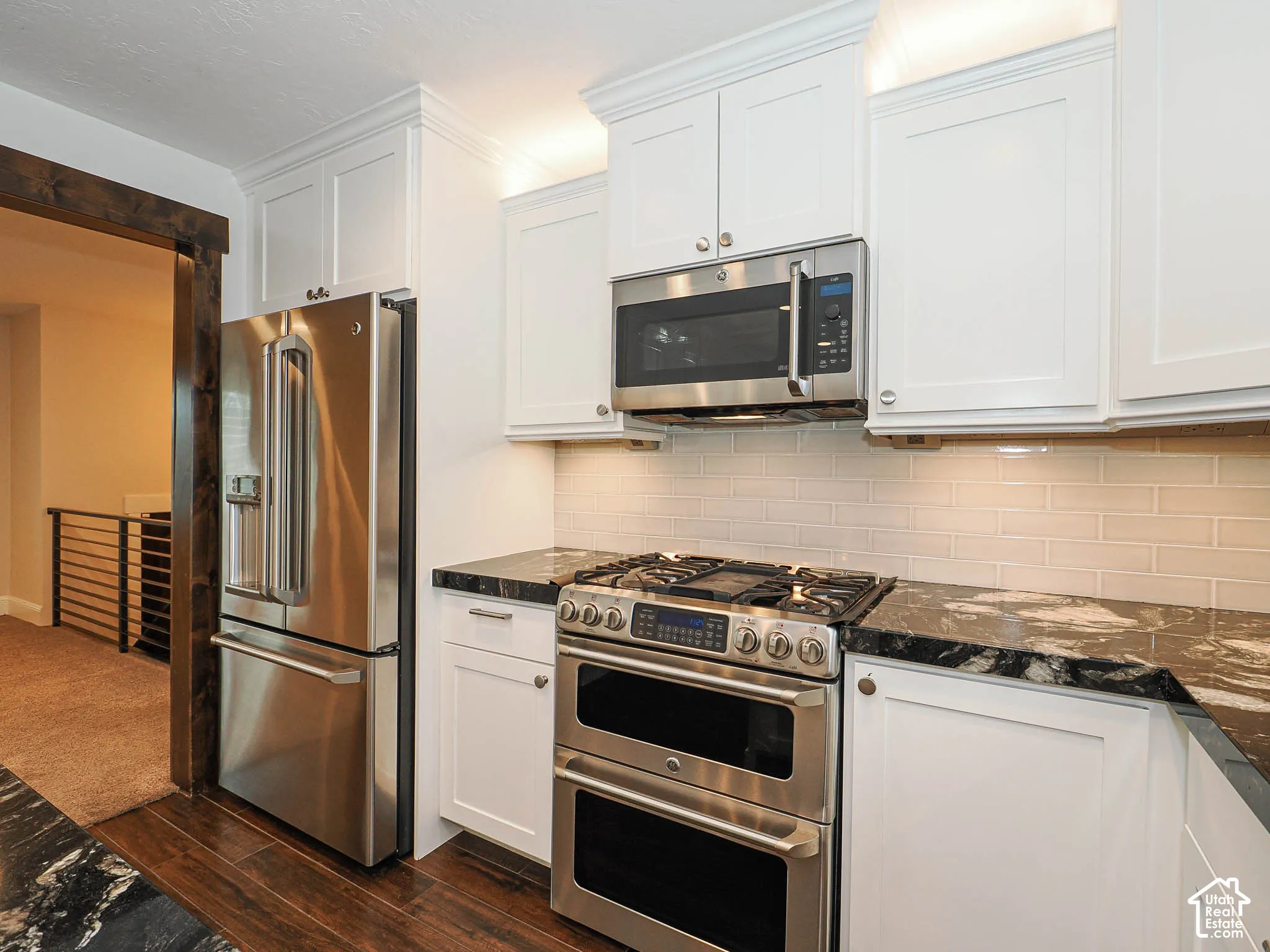 Stainless steel double oven range, stainless steel refrigerator, white shaker-style cabinetry, dark stone countertops, and a subway tile backsplash