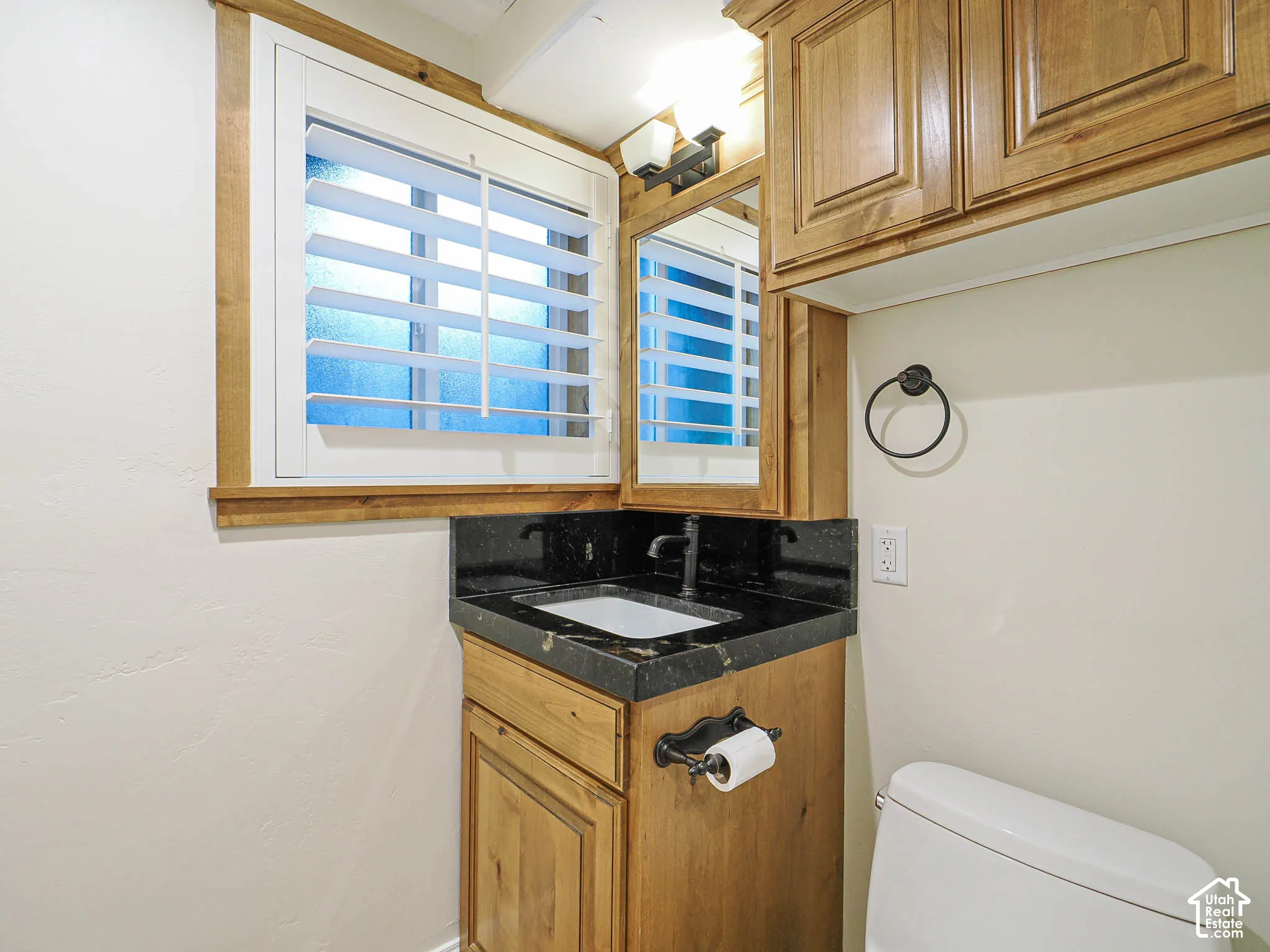 Wood-finish vanity with a dark countertop and integrated sink, complemented by a wall-mounted mirror