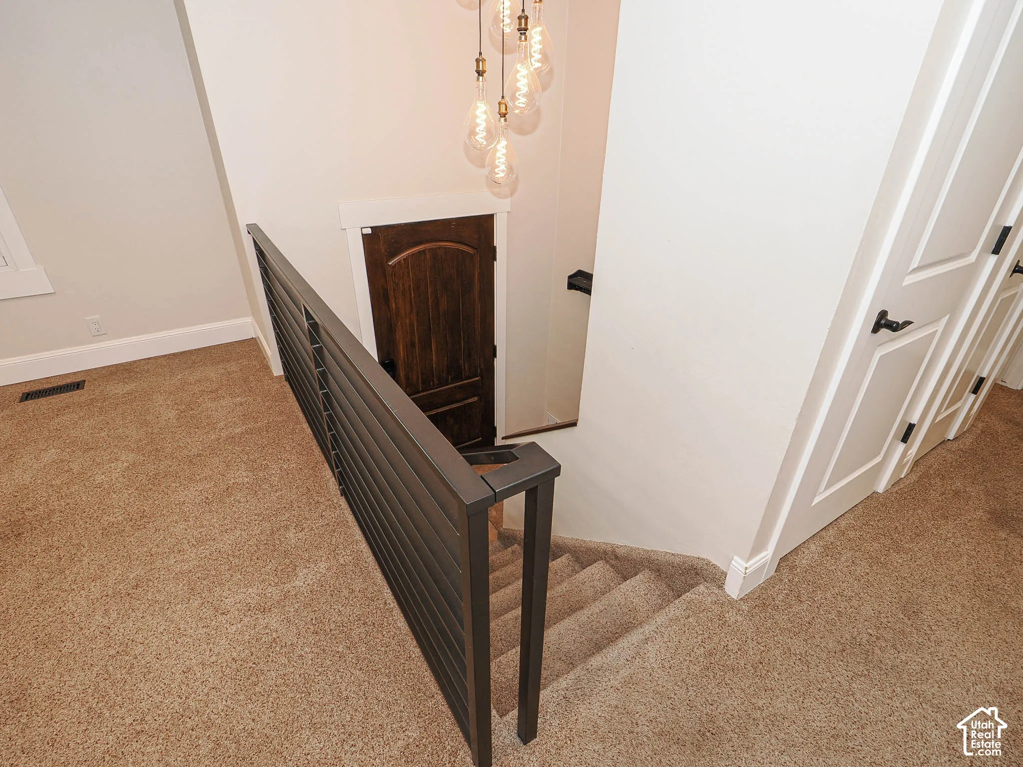 Staircase featuring dark metal railing, carpeted treads, and a multi-bulb pendant light fixture
