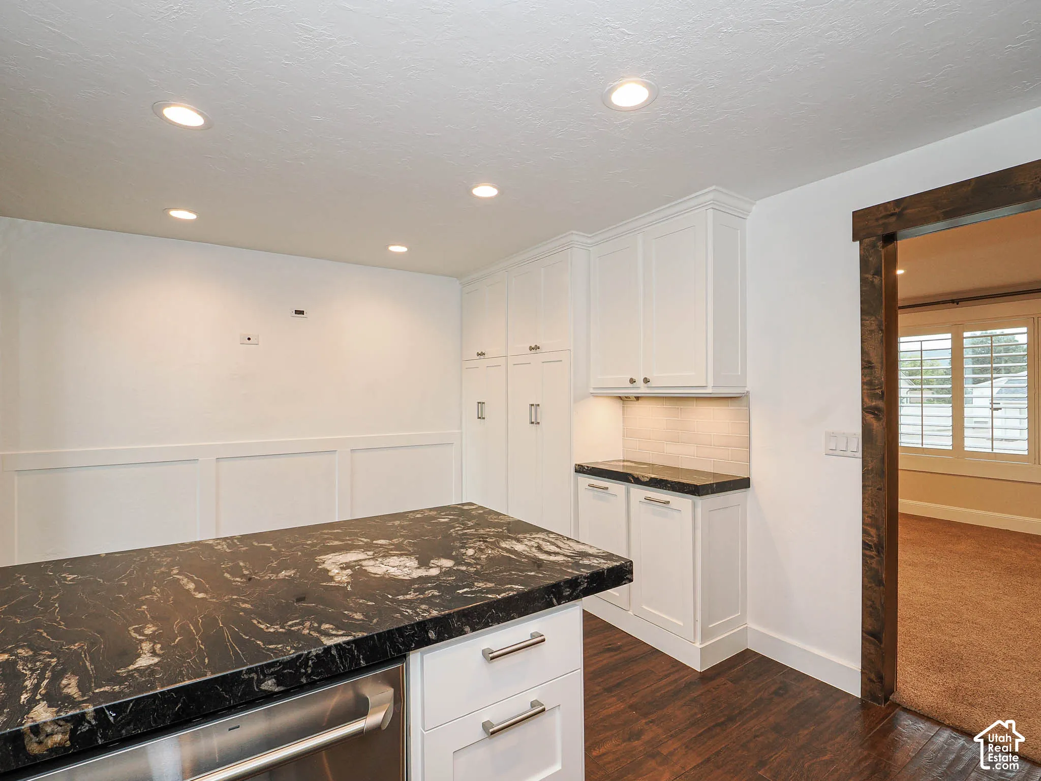 Recessed lighting, wood-finish flooring, white paneling, white cabinetry, and dark countertop surfaces