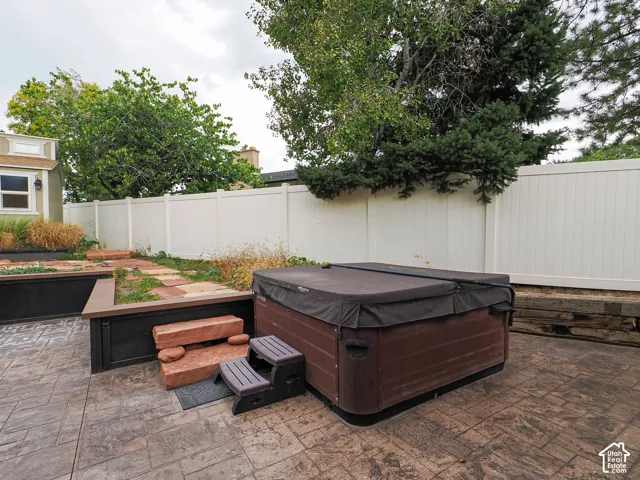 Private backyard space featuring a spa, stamped concrete patio, and a white privacy fence
